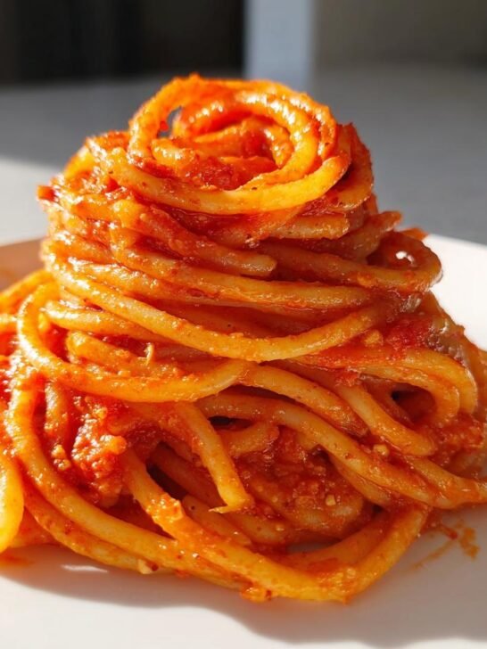 A tall, artistic swirl of spaghetti coated in a rich, creamy tomato garlic pasta sauce on a white plate.