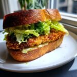 Close-up of a Crispy Chicken Caesar Sandwich featuring a golden fried cutlet, crisp lettuce, and sauce on thick, toasted bread.