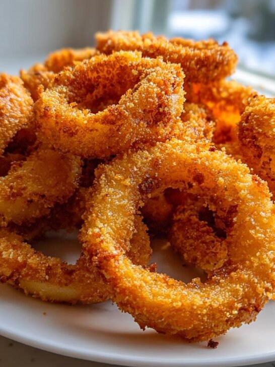 A pile of golden brown, crispy fried Tennessee Onions rings stacked high on a white plate.