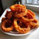 A tall stack of perfectly golden brown, crispy fried Tennessee Onions rings piled on a white plate.