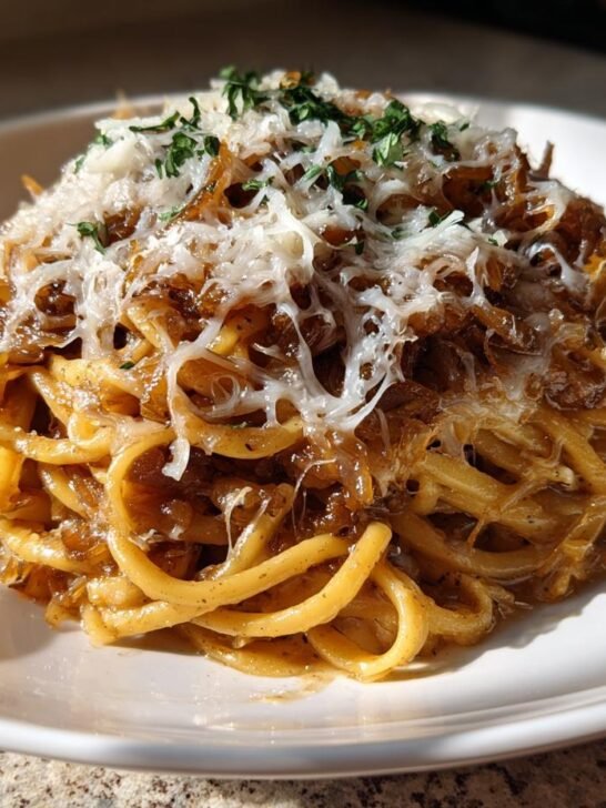 A serving of French Onion Pasta Recipe with caramelized onions, melted Gruyere, and parsley on a white plate.