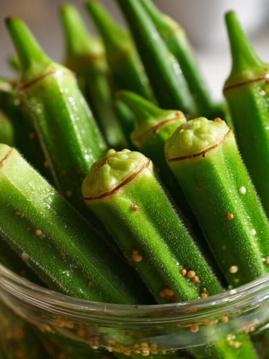 Close-up of fresh green okra pods standing upright in a glass jar, ready for making Pickled Okra.