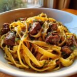 A close-up of a bowl filled with rich Garlic Steak Pasta featuring fettuccine noodles and cubed steak pieces.