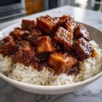 Close-up of glazed Ginger Lime Pork served over a bed of white coconut rice in a white bowl.