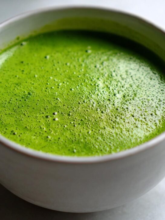 Close-up of vibrant Green Detox Soup with a frothy top served in a light-colored mug.