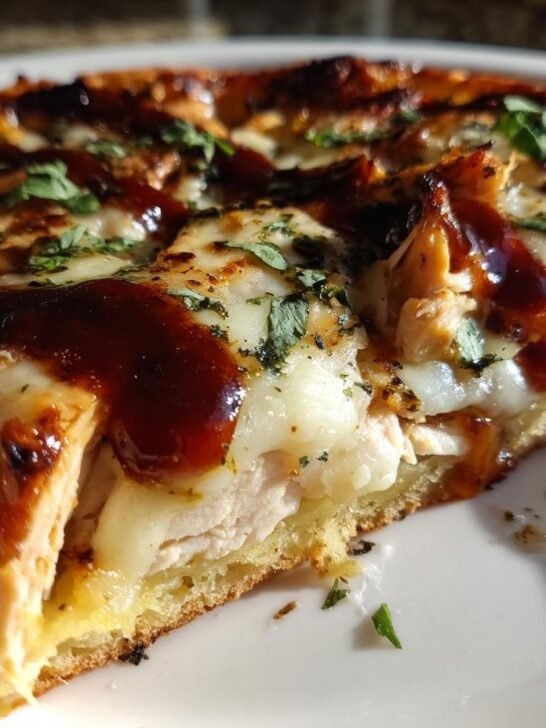 Close-up of a thick slice of Grilled Summer Bbq Chicken Pizza topped with melted cheese and BBQ sauce.
