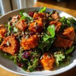 Close-up of a vibrant Harissa Roasted Sweet Potato Power Salad featuring orange sweet potato chunks, green leaves, quinoa, pumpkin seeds, and dried cranberries.