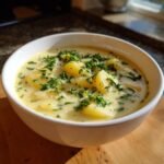 A close-up of a white bowl filled with Hearty Cheddar Garlic Herb Potato Soup, topped generously with fresh parsley.
