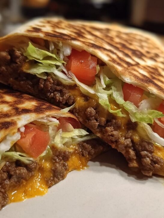 A homemade Crunchwrap Supreme, grilled and cut in half, showing seasoned ground beef, melted cheese, lettuce, and tomato.