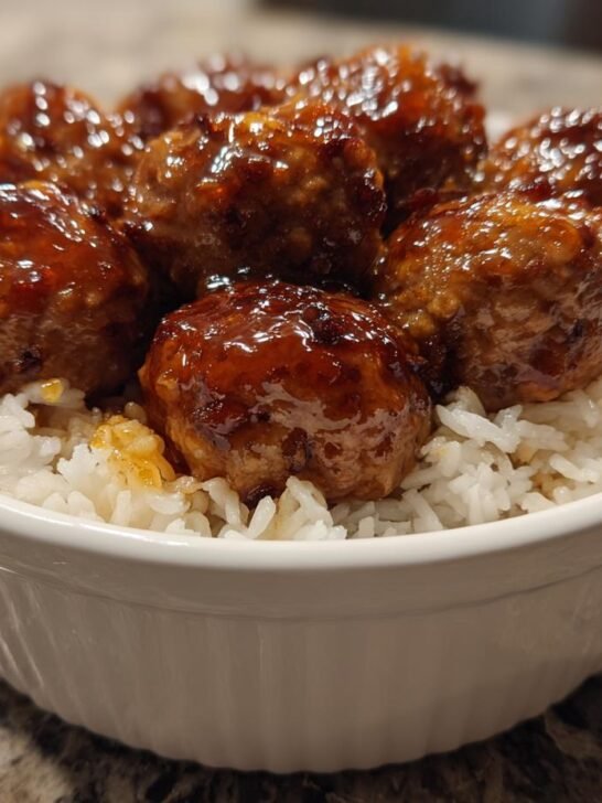 Close-up of glazed meatballs served over white rice in a white bowl, featuring the Honey Garlic Meatball Rice Bake.