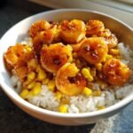 Close-up of a white bowl filled with white rice, topped with corn and glazed Honey Garlic Shrimp.