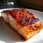 A perfectly cooked fillet of salmon topped with a thick, shiny Hot Honey Glazed Salmon coating featuring visible chili flakes.