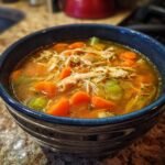 Close-up of a dark blue bowl filled with rich broth, shredded chicken, bright orange carrots, and celery chunks from the Instant Pot Chicken Vegetable Soup.