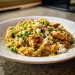 A close-up of Lemon Feta Chicken And Orzo mixed with green peas, topped with crumbled feta, lemon zest, and parsley.
