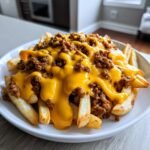 A close-up of crispy french fries smothered in chili and melted cheddar sauce, the perfect Loaded Cheese Fries Beef.