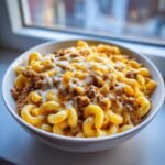 Close-up of a white bowl filled with Loaded Cheeseburger Pasta, featuring elbow macaroni, seasoned ground beef, and melted cheddar and white cheese.