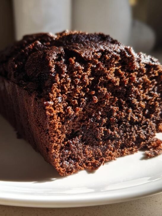 Close-up of a moist, dark slice of Chocolate Zucchini Cake resting on a white plate.