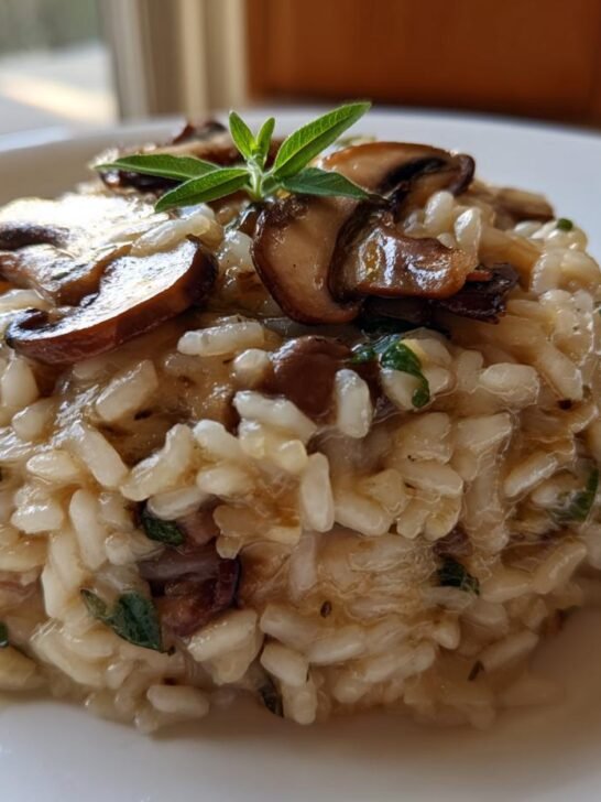 A perfectly plated serving of creamy Mushroom Sage Risotto topped with saut&eacute;ed mushrooms and a fresh sage sprig.