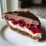 A decadent slice of Chocolate Cherry Cream Pie showing layers of crust, cream, cherries, and chocolate mousse topping.