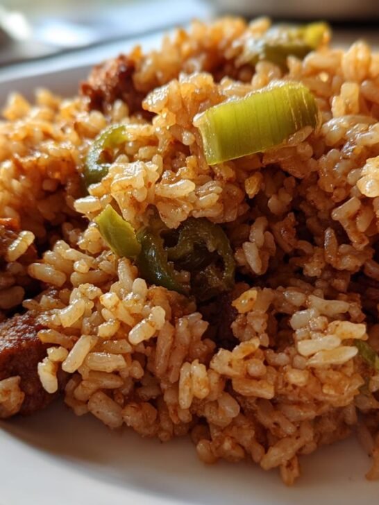A close-up shot of a serving of rich, brown One Pot Dirty Rice mixed with pieces of sausage and green peppers.