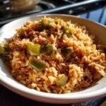 A close-up of a white bowl filled with flavorful One Pot Dirty Rice mixed with ground meat and large chunks of green bell pepper.