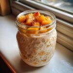 Close-up of Peach Cobbler Overnight Oats Recipe topped with diced peaches and cinnamon in a glass jar.