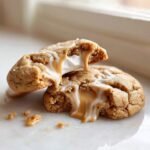 Close-up of a Peanut Butter Marshmallow Cookies broken in half, showing melted marshmallow and caramel sauce oozing out.