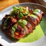 Close-up of sliced, roasted Peruvian Chicken With Green Sauce generously drizzled over the meat and pooled on a white plate.