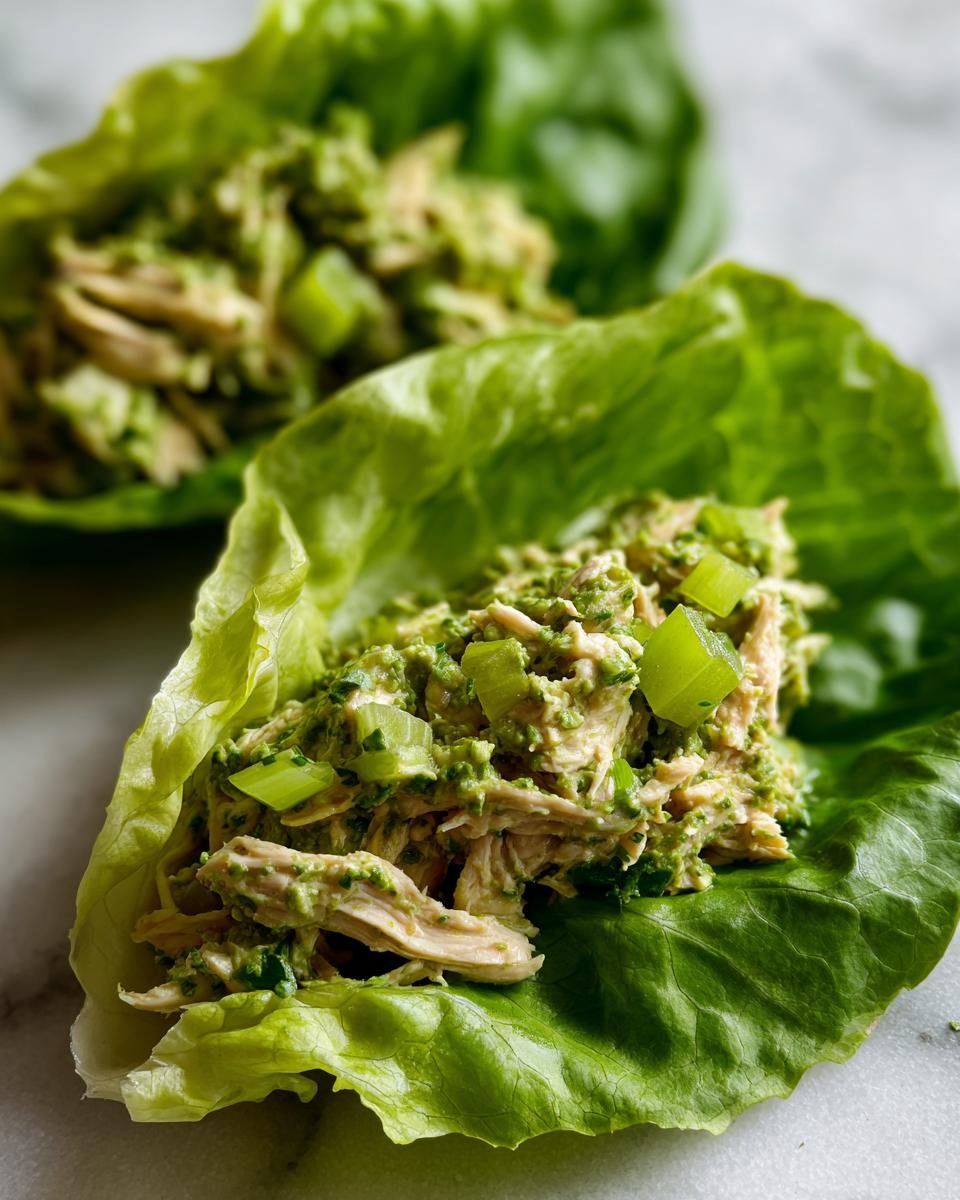 Close-up of shredded chicken mixed with green pesto and celery served in crisp lettuce cups for Pesto Chicken Lettuce Wraps.