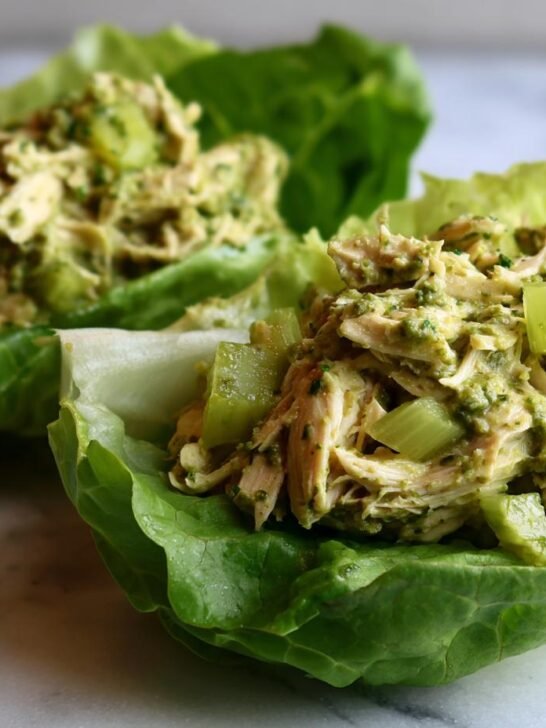 Two servings of Pesto Chicken Lettuce Wraps featuring shredded chicken mixed with green pesto and celery chunks in crisp lettuce cups.
