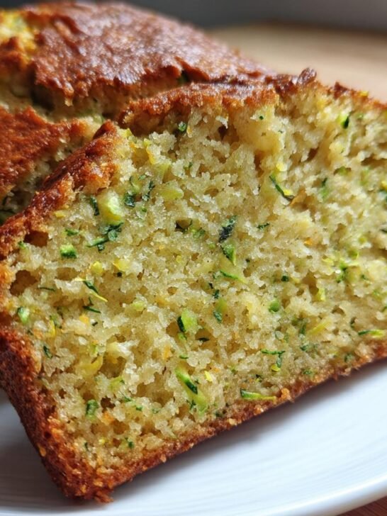 Close-up of a slice cut from a golden-brown Pineapple Zucchini Bread Loaf, showing moist crumb and green zucchini shreds.