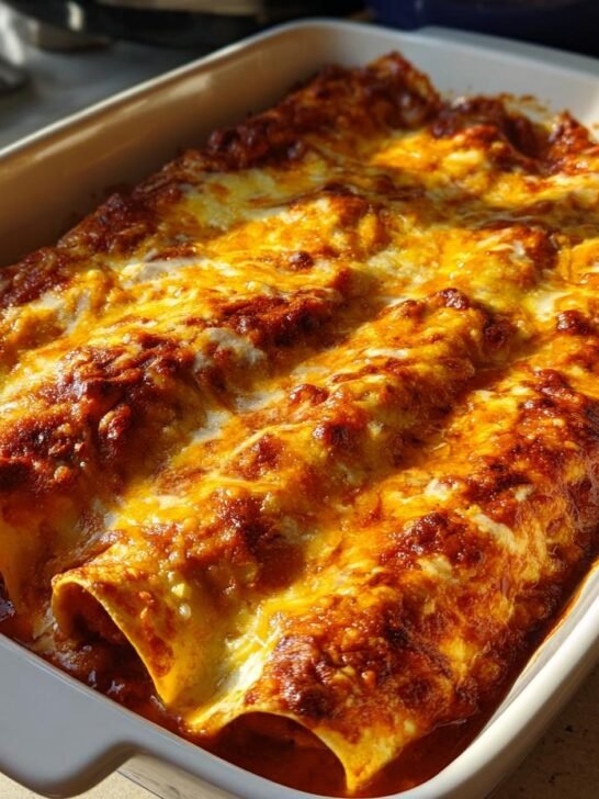 Close-up of baked Pizza Enchiladas Ground Beef rolls covered in melted, bubbly cheese and rich sauce in a white baking dish.