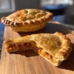 Close-up of a Pizza Pot Pies half showing flaky crust and cheesy, saucy filling next to a whole pot pie.