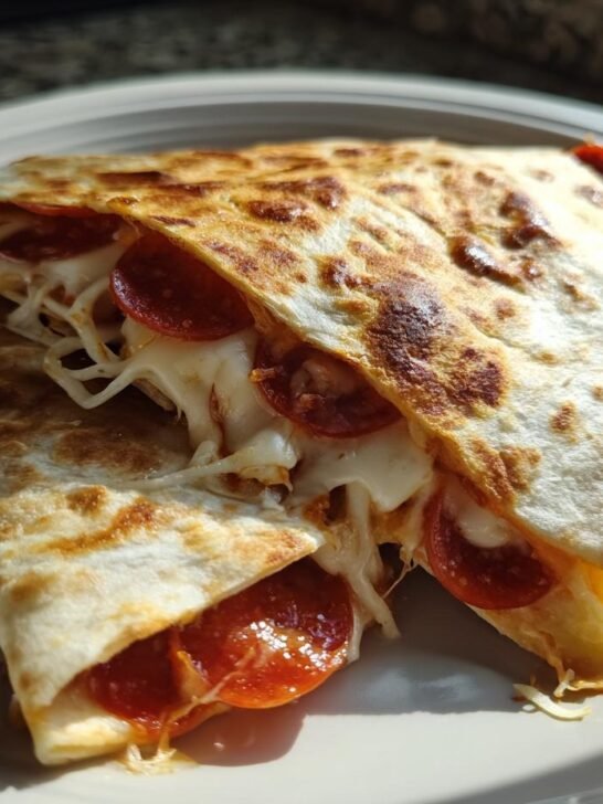 Close-up of two folded Pizza Quesadillas With Pepperoni showing melted cheese and pepperoni oozing out.