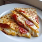 Close-up of three stacked slices of golden-brown Pizza Quesadillas With Pepperoni oozing melted cheese.