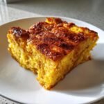 A square slice of rich, golden Pumpkin Bread Pudding Recipe with a caramelized top, served on a white plate.