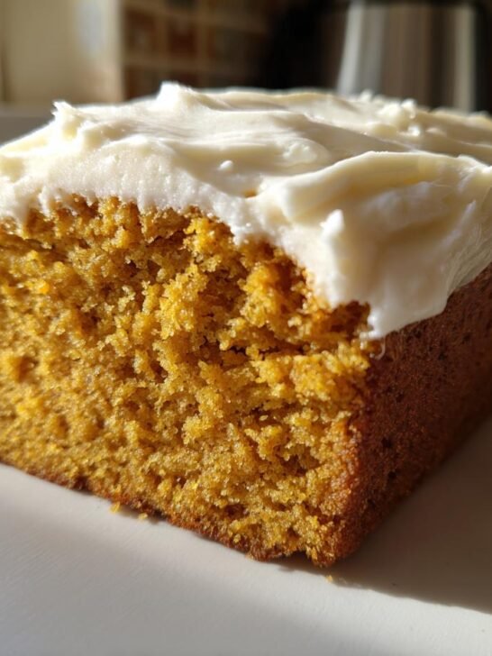 Close-up of a moist slice of Pumpkin Bread With Cream Cheese Frosting sitting on a white surface.