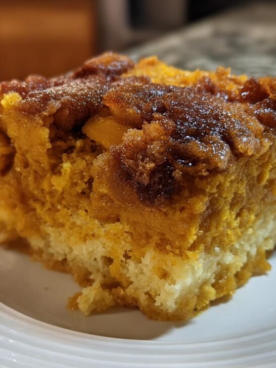 A close-up of a moist slice of Pumpkin Spice Dump Cake showing the orange pumpkin layer over a light cake base.