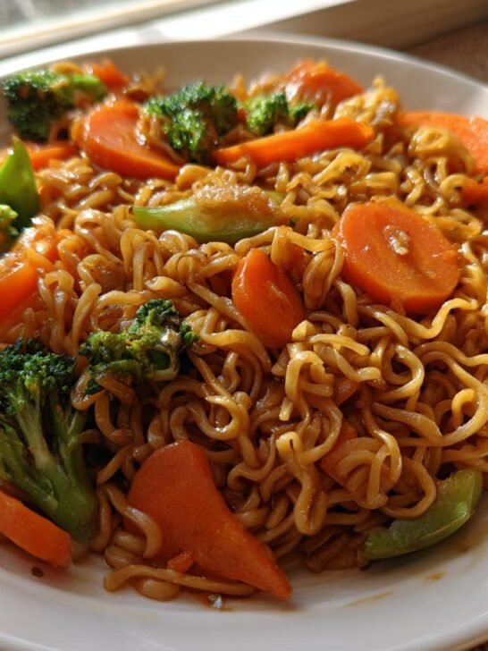 A close-up of a plate featuring a savory Ramen Noodle Stir Fry mixed with bright green broccoli florets and sliced carrots.