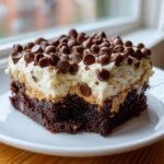 A rich square of Reeses Peanut Butter Earthquake dessert with a brownie base, peanut butter layer, and whipped topping covered in chocolate chips.