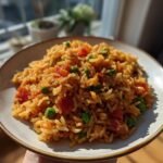 A close-up of a bowl filled with fluffy Restaurant Style Mexican Rice mixed with diced tomatoes and green peas.