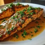 Close-up of a pan-seared Salmon Meuniere fillet covered in brown butter sauce and fresh parsley.