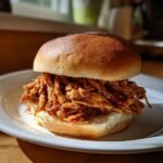 Close-up of a juicy, saucy pile of shredded chicken sandwiches on a soft bun.