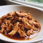 A close-up of shredded chicken coated in a rich, brown peanut sauce from the Slow Cooker Peanut Chicken Recipe.