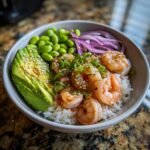 Close-up of a vibrant Shrimp Poke Bowl featuring seasoned shrimp over rice, topped with avocado, edamame, and red onion.