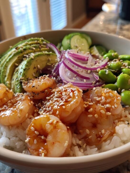 A close-up of a ready-to-eat Shrimp Poke Bowl featuring glazed shrimp, avocado, edamame, and red onion over rice.