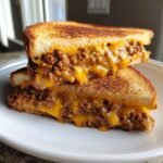 Two halves of a toasted Sloppy Joe Grilled Cheese stacked, showing melted cheddar cheese and savory ground meat filling.