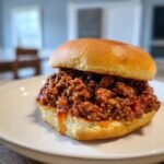 Close-up of a fully loaded Sloppy Joe Recipe Easy sandwich on a soft bun, served on a white plate.