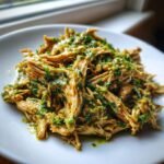 Close-up of shredded Slow Cooker Cilantro Lime Chicken coated in a vibrant green cilantro-lime sauce.