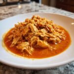 A close-up of shredded chicken coated in a rich, orange-red sauce, representing Slow Cooker Creamy Tomato Basil Chicken.